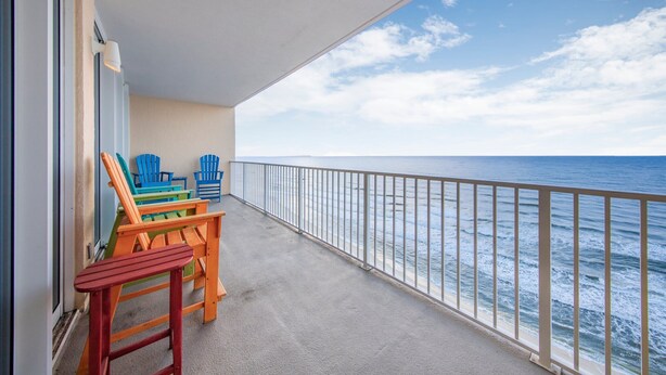 A balcony with a view of the ocean, featuring a railing and a few colorful chairs.