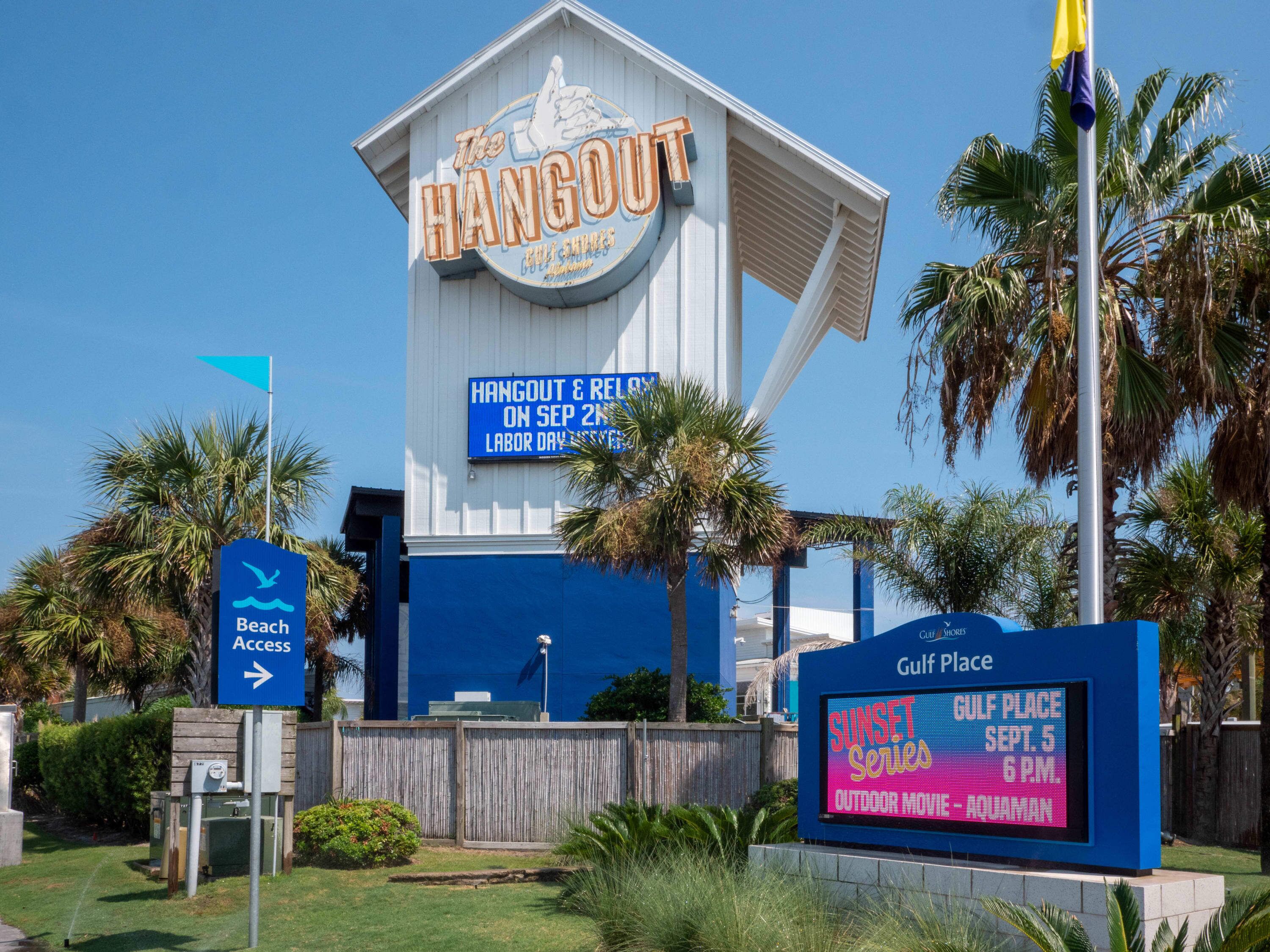 A building with a sign reading "The Hangout" and another sign indicating "Gulf Place Sunset Series" with an outdoor movie showing.