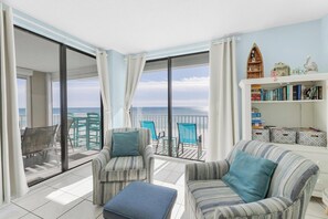 Un balcon avec vue sur la mer, aménagé avec des chaises à rayures et un canapé, ainsi qu’une bibliothèque contenant des livres et des objets décoratifs.