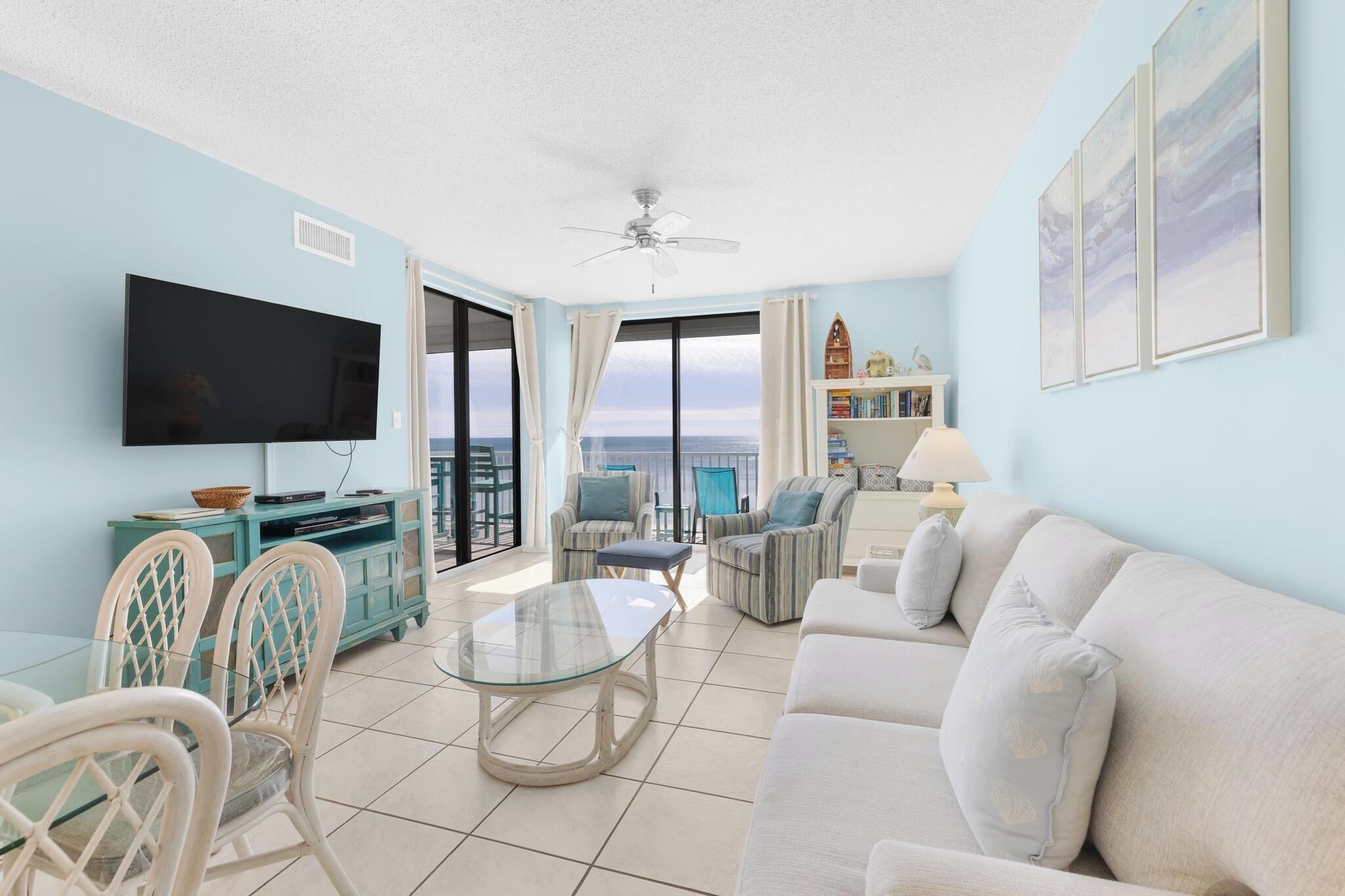 A living room with a TV, seating, a balcony with a view, and a ceiling fan.