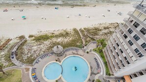 Un hotel con zona de piscina que incluye dos piscinas circulares y vista a la playa.