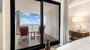Habitación de hotel con un amplio ventanal corredero que da a un balcón con mobiliario exterior.