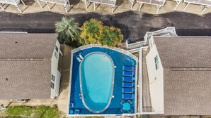 An aerial view of a hotel with a swimming pool surrounded by lounge chairs, a parking area, and a street with houses. - 🐶Pet Friendly Condo with Pool-Steps to the Beach-Sea & Sun 204🌴 (Gulf Shores)