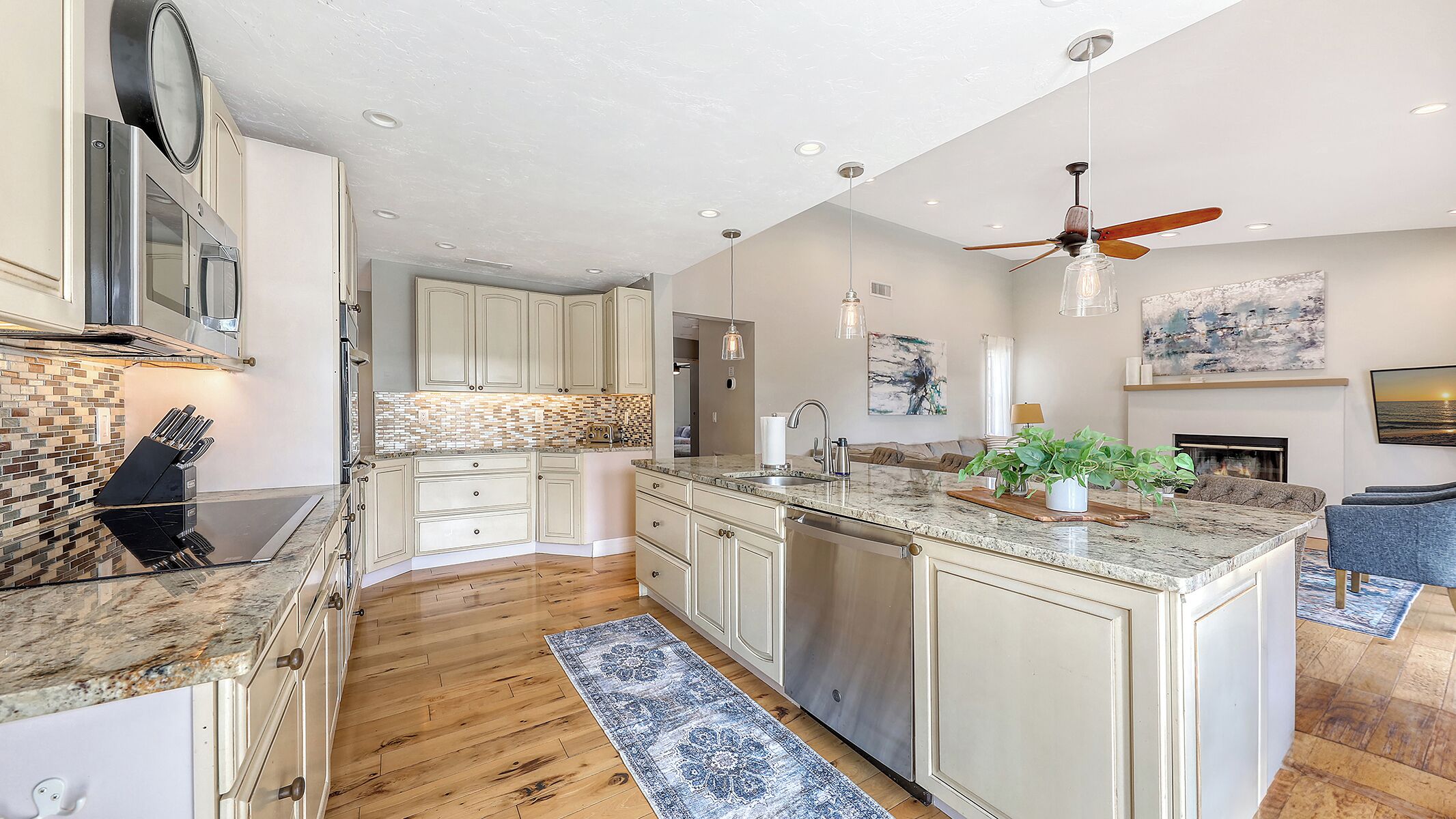 A modern kitchen with a central island, wooden flooring, and a ceiling fan.