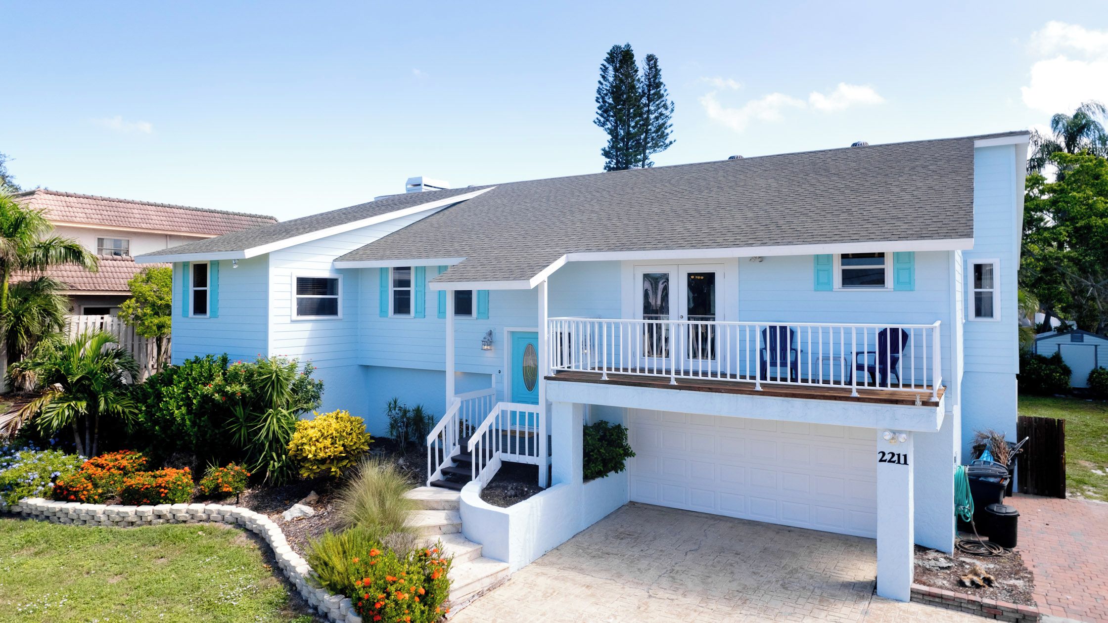 A two-story residential building with a front porch, a garage, and a well-maintained garden.