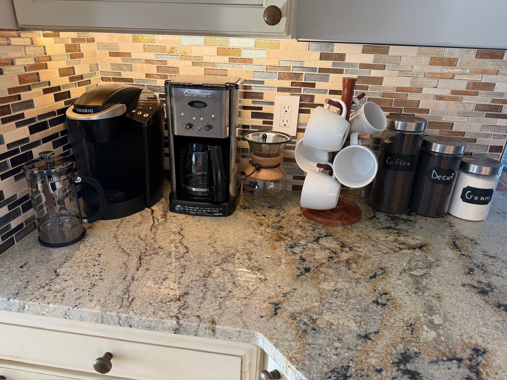 Una cocina con cafetera, Keurig, molinillo de café y recipientes etiquetados para café, descafeinado y crema.