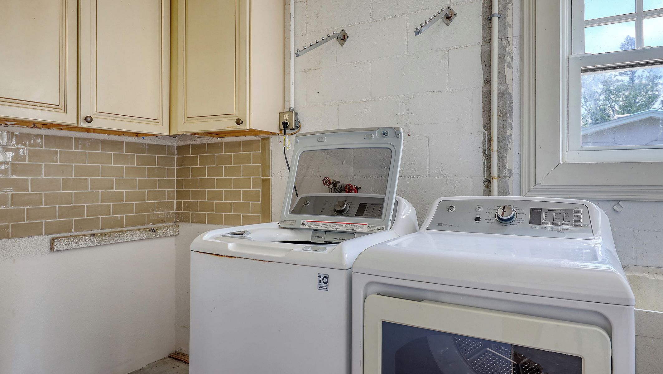A laundry room with two washing machines, a tiled backsplash, and wooden cabinets.