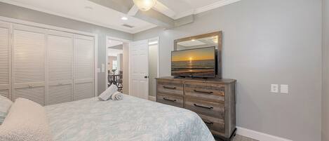 A bedroom with a bed, a dresser, a ceiling fan, and a TV displaying a sunset.