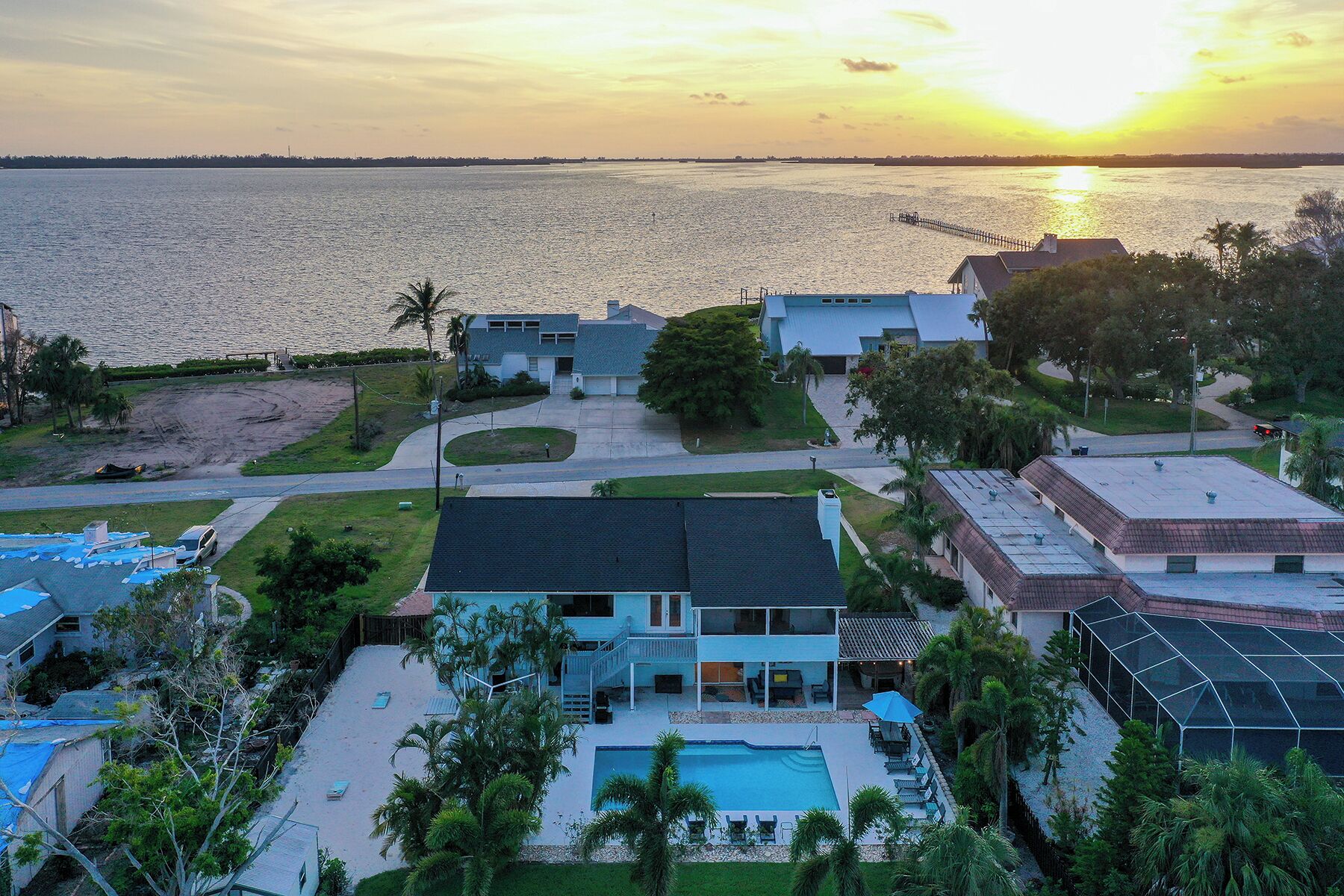 A residential area with a large swimming pool, multiple houses, and a pier extending into the water.