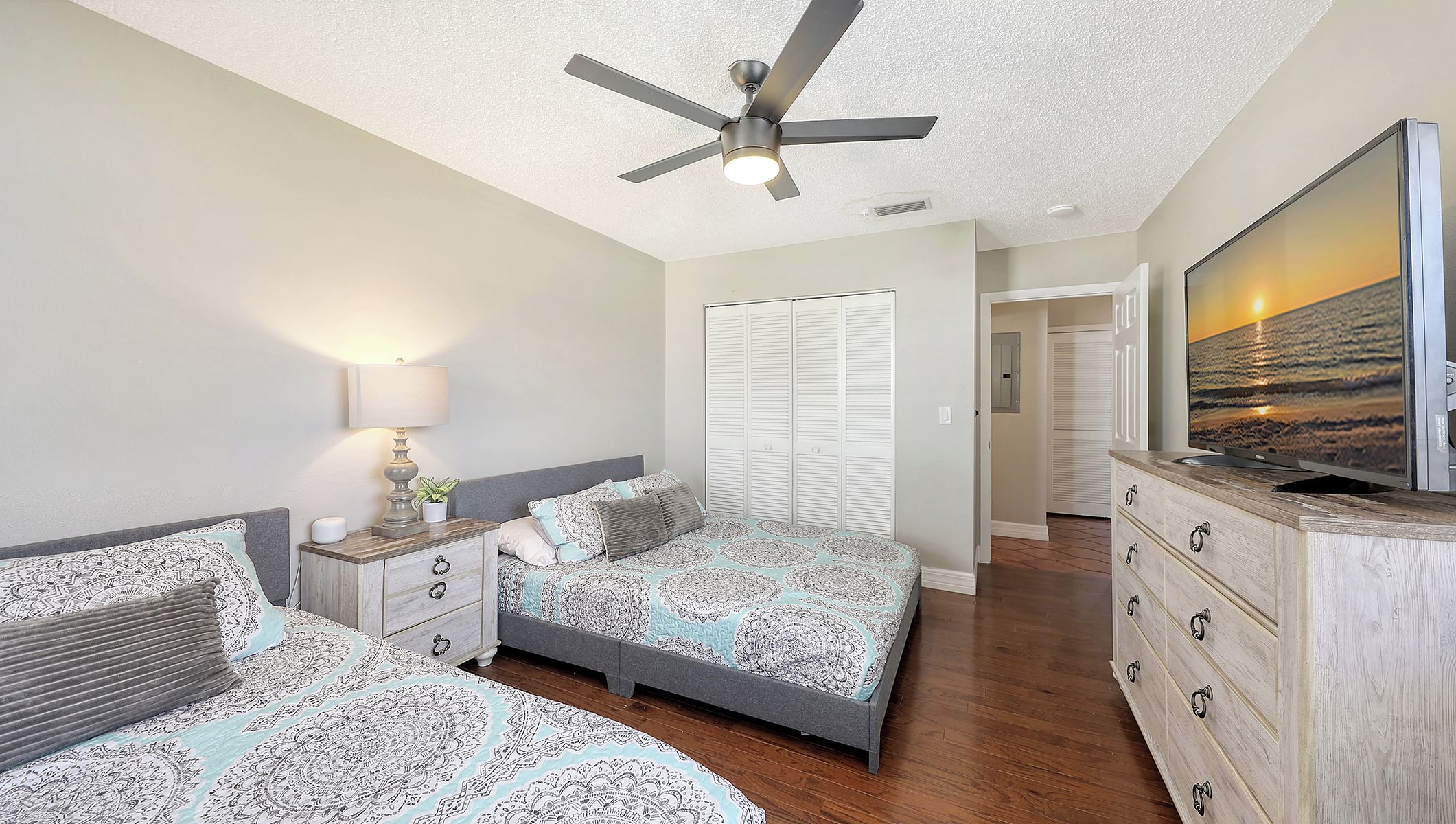A bedroom with a bed, nightstands, a dresser, a ceiling fan, and a TV.