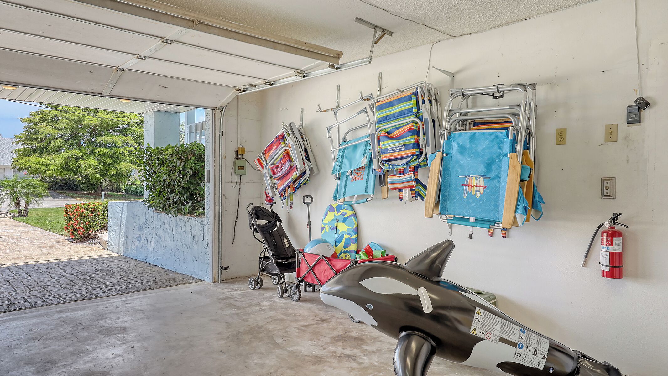 A garage with a concrete floor, a stroller, and various colorful bags hanging on the wall.