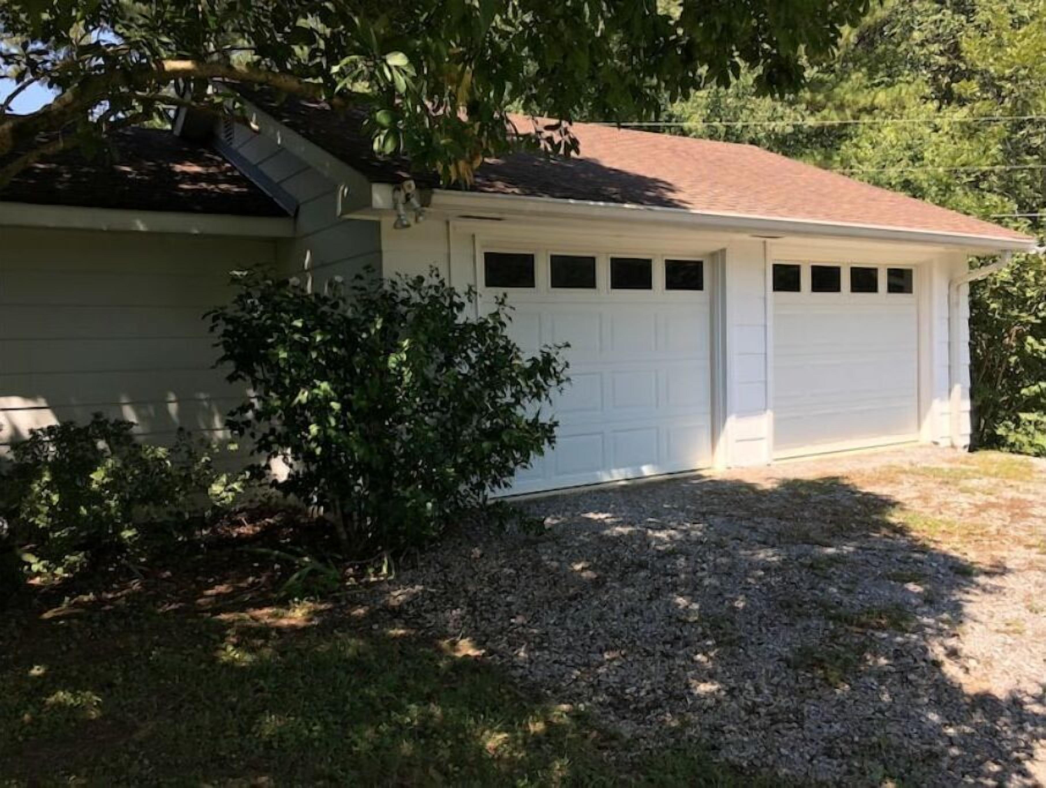 Une maison de plain-pied avec une porte de garage blanche, un toit en pente et une allée gravillonnée.