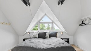A bedroom with a sloped ceiling, a bed with a grey quilt, two bedside tables with lamps, and a window with a view of trees. - Stunning home in Hurup Thy with WiFi (Hurup Thy)