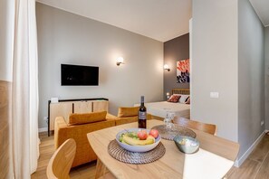 A modern hotel room with a dining area, a TV mounted on the wall, and a bed with a colorful headboard.
