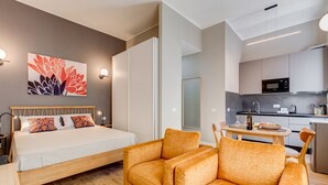 Una habitación de hotel moderna con cama, sofá, mesa de comedor, zona de cocina y una obra de arte en la pared.