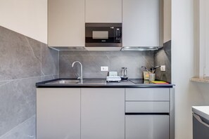 A modern kitchen with grey cabinets, a stainless steel sink, and a built-in microwave.