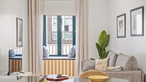 A modern living room with a sofa, a dining table, and chairs. There is a window with a view of a balcony. - In downtown Funchal, Tanoeiros Residence II (Funchal)