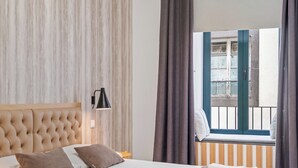 A hotel room with a large bed, a window with a view of the outside, and a wall-mounted lamp. - In downtown Funchal, Tanoeiros Residence II (Funchal)