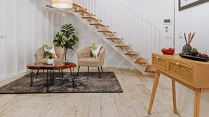 Un salon moderne avec un escalier en bois, deux fauteuils, une table basse, une plante en pot et une petite table ornée d’objets décoratifs.