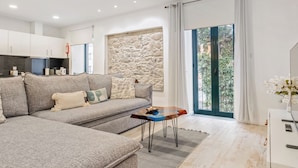 Un salon moderne avec un canapé d’angle gris, une petite table en bois et un mur décoratif en pierre.