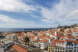 A coastal cityscape with historic buildings, a prominent church tower, and a view of the sea.