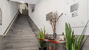 Un moderno vestíbulo de hotel con una escalera de baldosas grises, plantas en macetas y una pequeña mesa con objetos decorativos.