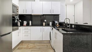 Una cocina moderna con armarios blancos, encimera negra y lavadora integrada.