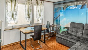 A room with a wooden desk, two chairs, a grey sofa, and a large window with curtains.