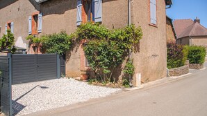 A residential building with a gravel driveway, a gated entrance, and a brick wall with climbing plants.