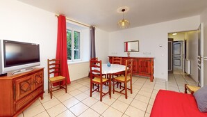 A room with a TV, wooden dining table, chairs, a red sofa, and a window with curtains.