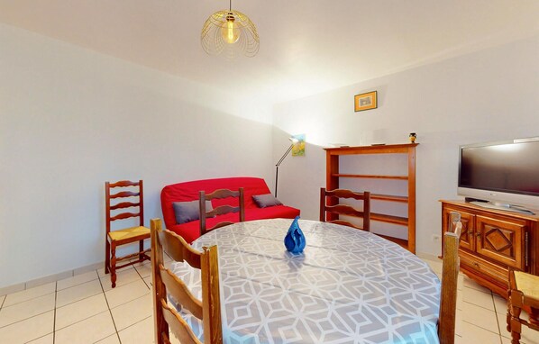 A compact living space with a dining table, a red sofa, a TV, and a wooden cabinet. - Stunning apartment in Trouvans with WiFi (Trouvans)