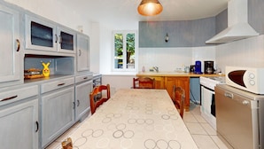 A kitchen with a dining table, cabinets, a stove, and a coffee maker.