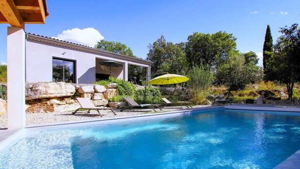 Ein modernes Haus mit Pool, Außenbereich mit Sitzgelegenheiten und einer Pergola mit Sonnenschirm.
