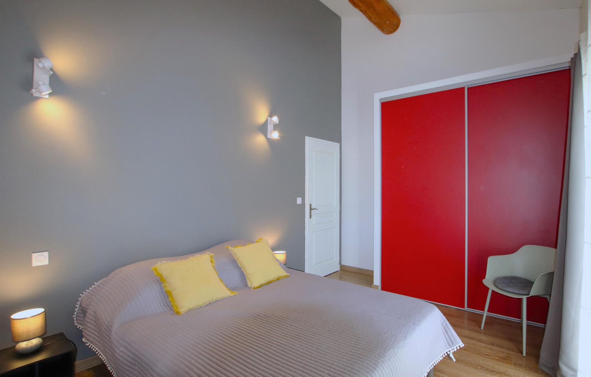 Ein Schlafzimmer mit einem Bett, zwei Nachttischlampen, einem roten Kleiderschrank und einem Sessel.