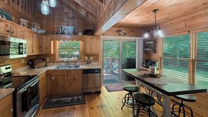 Interior de una cabaña de madera con cocina, comedor y ventanas amplias.