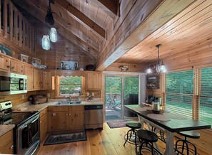 A wooden cabin interior with a kitchen, dining area, and large windows. - Cabin with a Creek   Screened porch.  Pet Friendly (Blue Ridge)