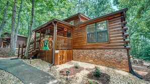 Une cabane rustique en rondins de bois, avec des fondations en pierre, une véranda en bois et une brouette.