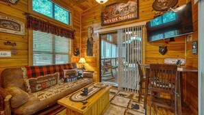 L’intérieur d’une cabane est décoré de bois, il y a un canapé orné d’une pancarte « Bienvenue dans la cabane », un téléviseur et des éléments de décoration sur le thème des ours.