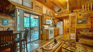 L’intérieur chaleureux d’un chalet, avec un décor en bois, un coin repas, une cuisine et un salon comprenant un canapé et une cheminée.