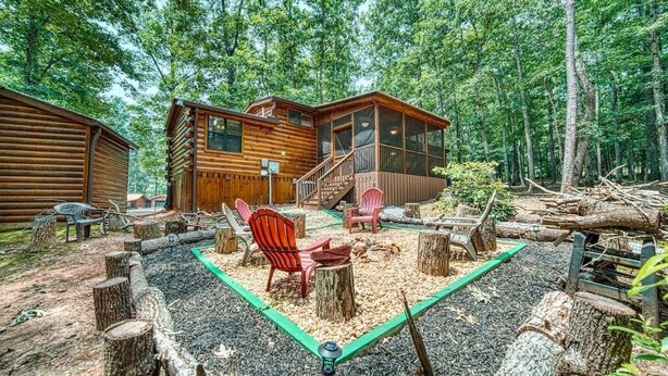 Une cabane dotée d’une terrasse et d’un foyer extérieur, le tout entouré de souches d’arbres et de gravier.