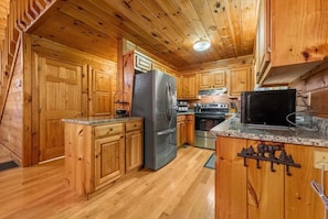 A wooden cabin kitchen with a refrigerator, stove, microwave, and wooden cabinets.