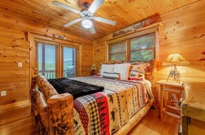 A wooden cabin bedroom with a bed, a ceiling fan, and a nightstand with a lamp.