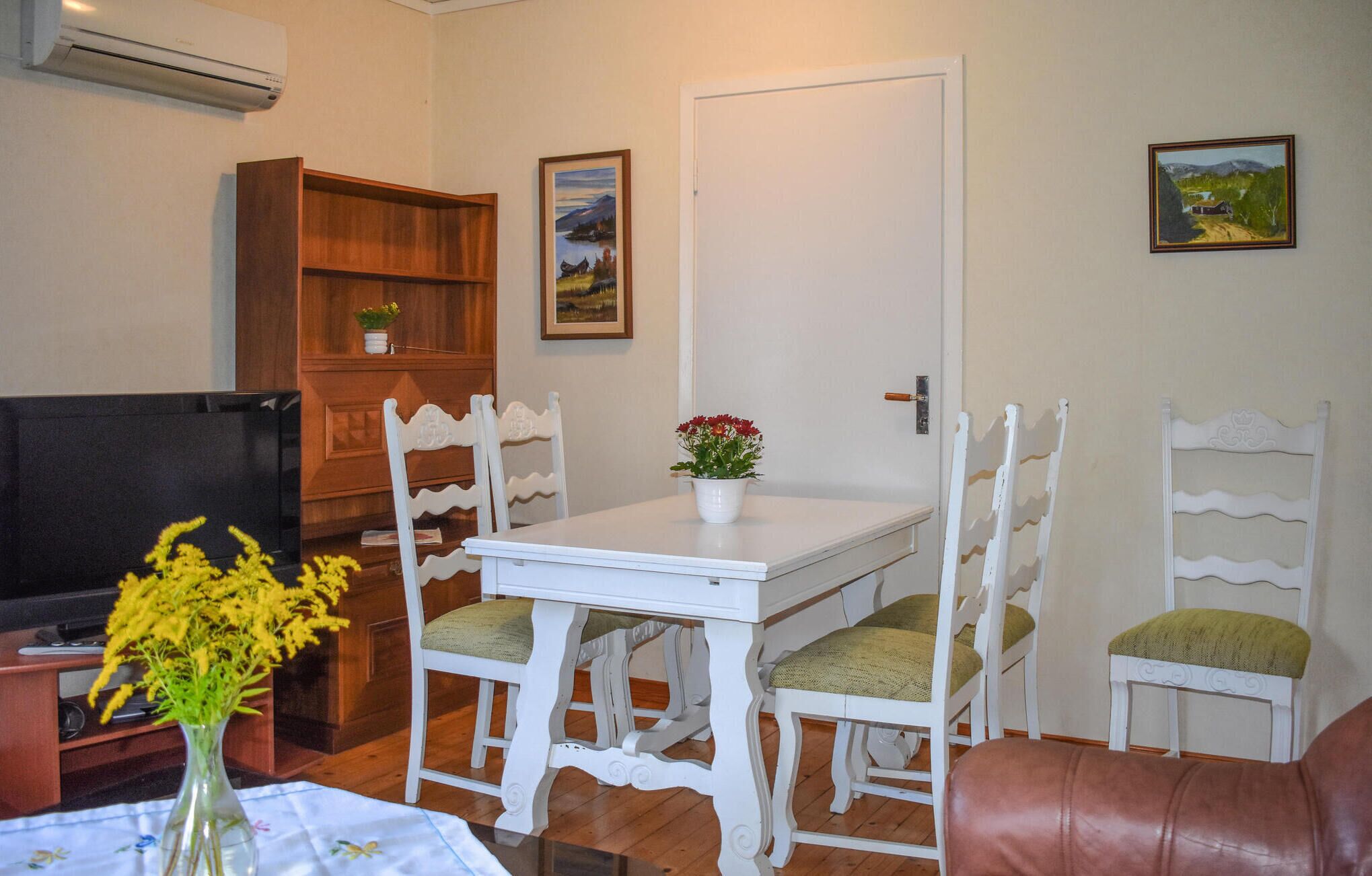 A dining area with a white table and chairs, a wooden bookshelf, and a TV.