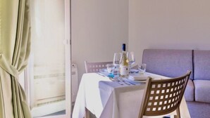 A dining area with a table set for two, a bottle of wine, and glasses. - Studio apartment of approximately 20 m2 composed of a living room with kitchenette equipped with 2 induction hobs, small fridge, sink,satellite TV and sofa.Sleeping area separated by sliding door with double bed, bathroom with shower without window.Air c (Marina di Cecina)