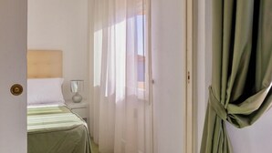 A bedroom with a bed, a bedside table, a lamp, and sheer curtains. - Studio apartment of approximately 20 m2 composed of a living room with kitchenette equipped with 2 induction hobs, small fridge, sink,satellite TV and sofa.Sleeping area separated by sliding door with double bed, bathroom with shower without window.Air c (Marina di Cecina)