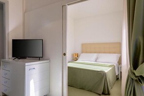 Habitación de hotel con cama, televisor en una cómoda y puerta que conduce a otra habitación.