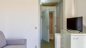 A room with a grey sofa, a white dresser with a TV, and a door leading to another room. - Studio apartment of approximately 20 m2 composed of a living room with kitchenette equipped with 2 induction hobs, small fridge, sink,satellite TV and sofa.Sleeping area separated by sliding door with double bed, bathroom with shower without window.Air c (Marina di Cecina)