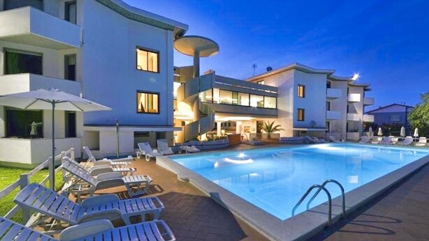 A modern hotel with a swimming pool, lounge chairs, and a well-lit outdoor area. - Studio apartment of approximately 20 m2 composed of a living room with kitchenette equipped with 2 induction hobs, small fridge, sink,satellite TV and sofa.Sleeping area separated by sliding door with double bed, bathroom with shower without window.Air c (Marina di Cecina)