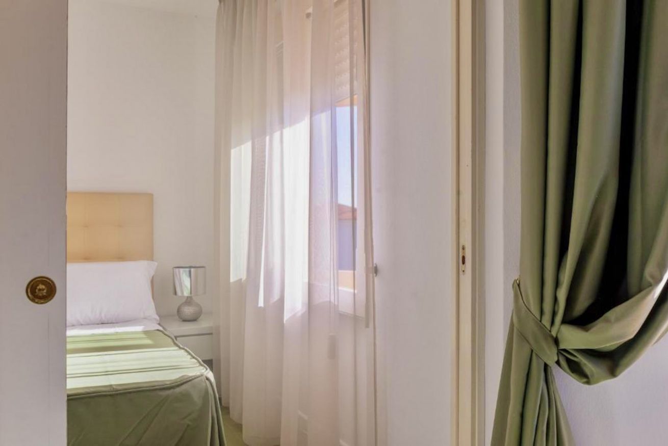Une chambre à coucher avec un lit, une table de chevet, une lampe et des rideaux légers.