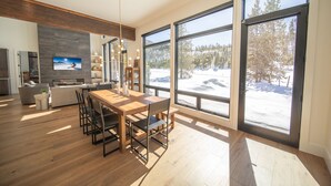 Una cocina moderna con una mesa y sillas de madera, ventanas amplias con vistas nevadas y una chimenea.